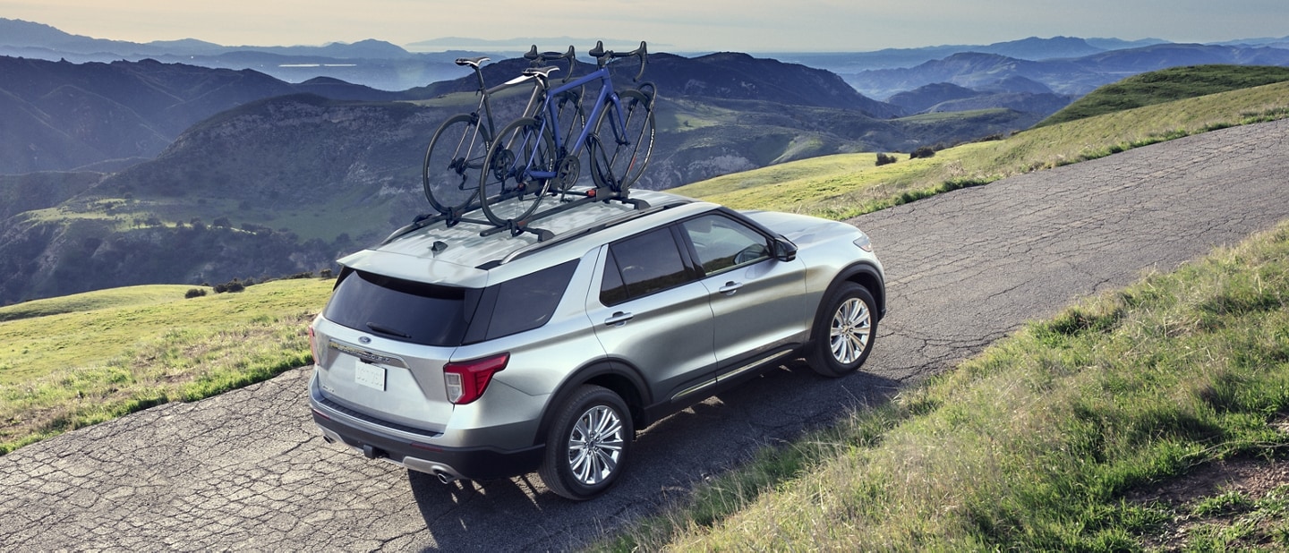 2022 Ford Explorer in Iconic Silver being driven along a mountain road with bikes on the roof