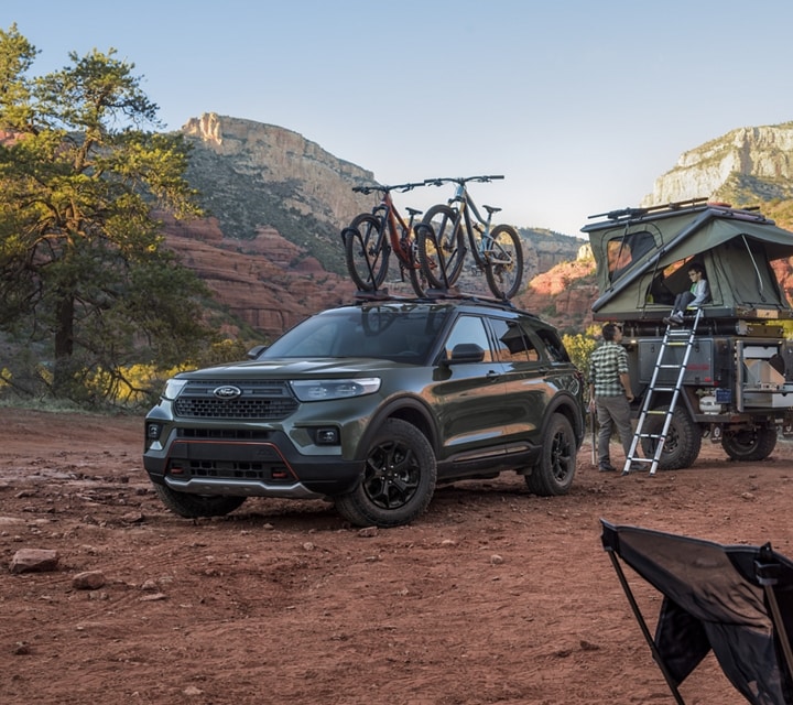 2023 Ford Explorer® Timberline® SUV in Forged Green Metallic parked in the desert with a trailer-top tent and family