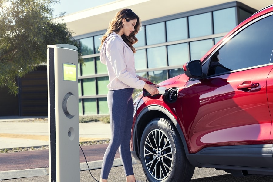 Woman at a public station charging a 2022 Ford Escape plug in hybrid model in Rapid Red Metallic extra cost color