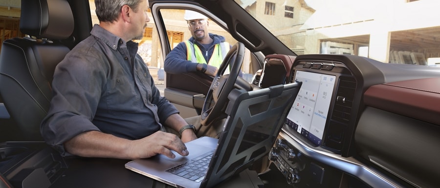 A person in a parked 2022 Ford F-150 using his laptop