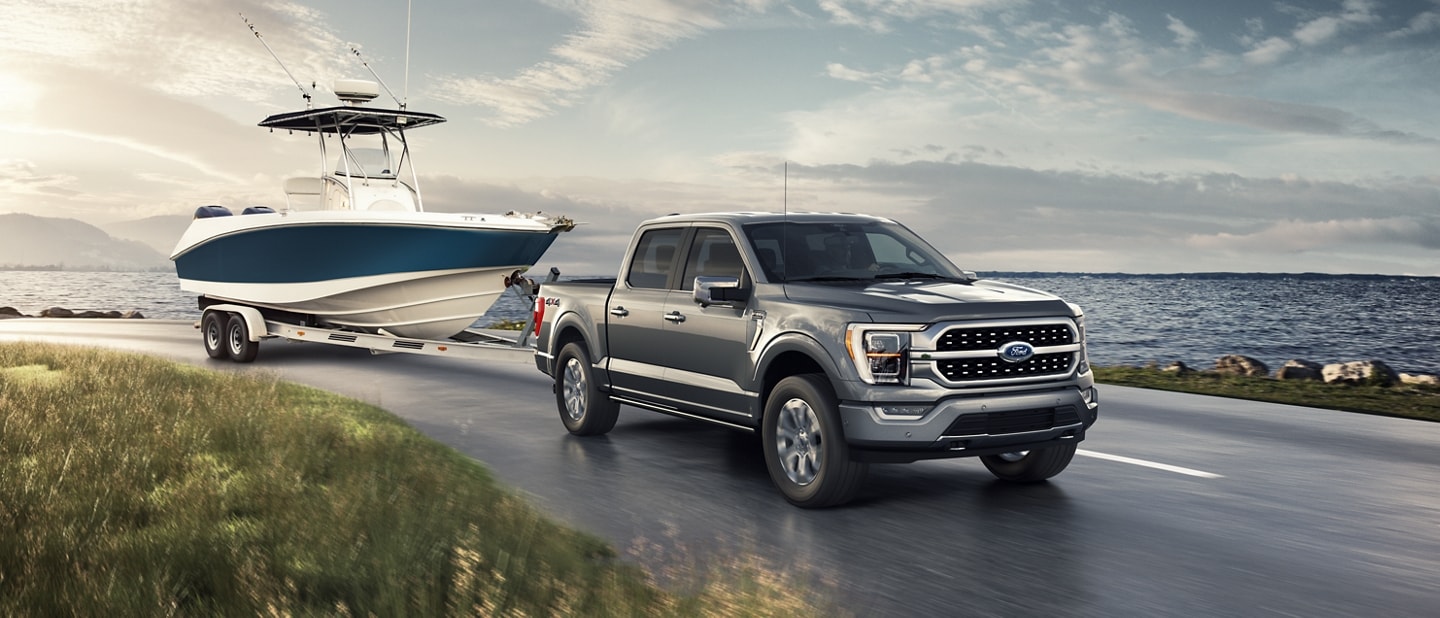 Stone gray 2022 Ford F-150® towing a large boat around a curve along the waterfront