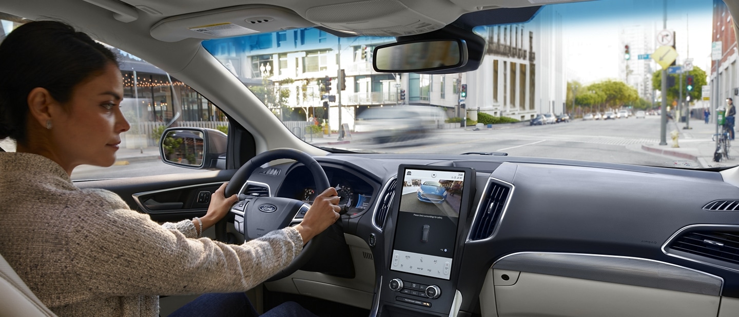 Interior view of a 2023 Ford Edge® center console as a woman driving glances at touchscreen