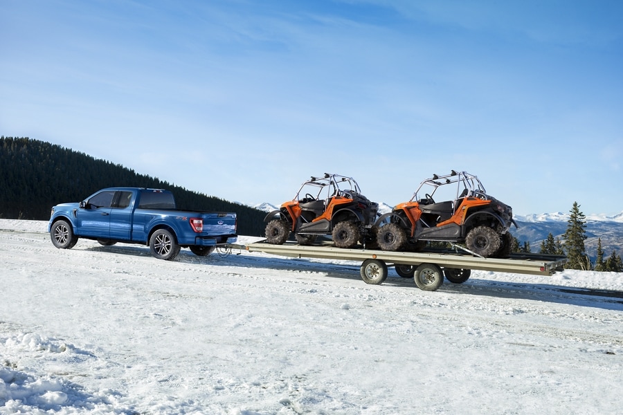 A 2022 Ford F-150 towing two tractor trucks in the snow
