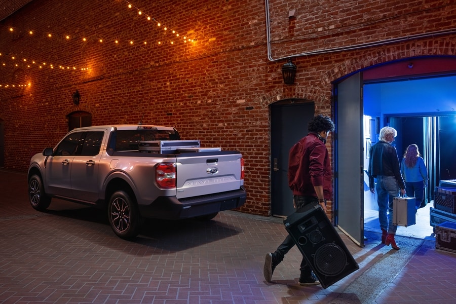 2023 Ford Maverick® truck in Iconic Silver parked in an alley with musicians bringing gear into a nightclub