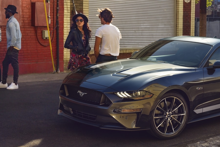 2023 Ford Mustang® coupe in Carbonized Gray Metallic parked on the street with four people standing nearby