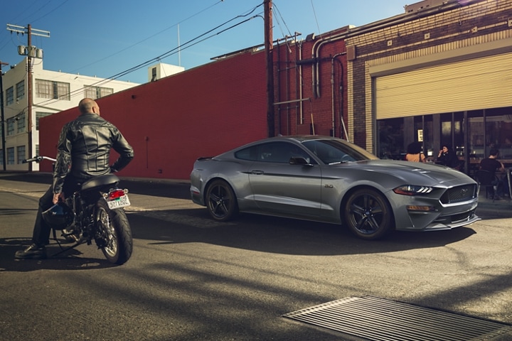 A person on a motorcycle admiring a 2023 Ford Mustang® coupe parked on a city street