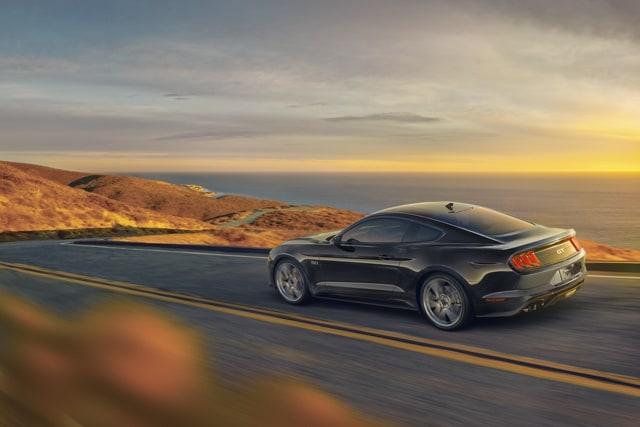 A 2023 Ford Mustang® coupe in Shadow Black being driven on an oceanside highway