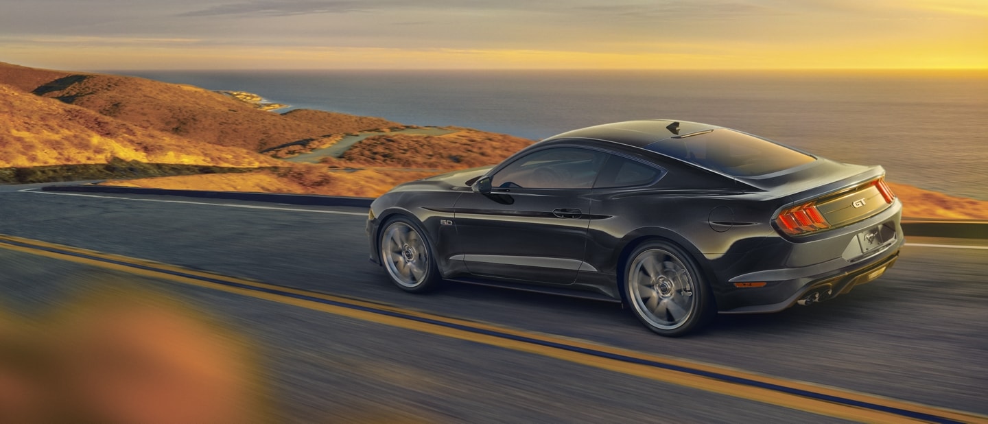 A 2023 Ford Mustang® coupe in Shadow Black being driven on an oceanside highway