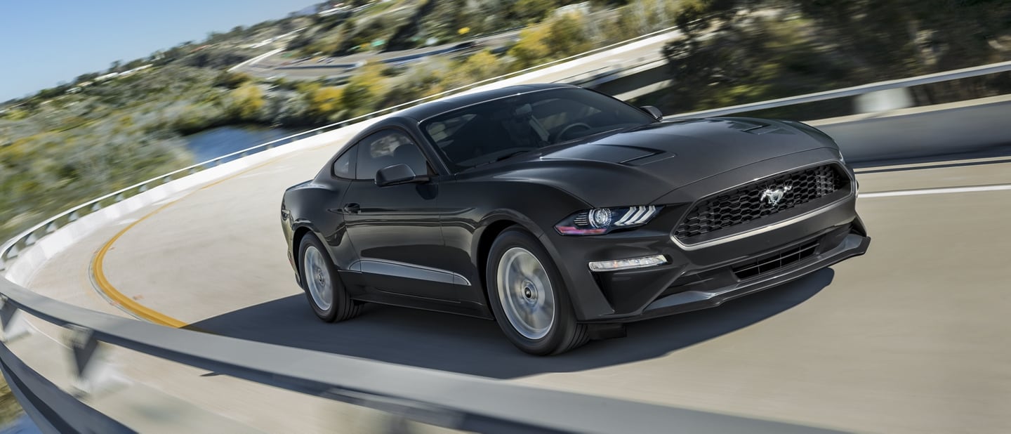 A 2023 Ford Mustang® coupe in Shadow Black being driven around a curve on a mountain road