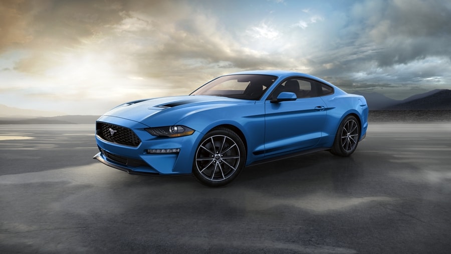 2023 Ford Mustang® coupe in Grabber Blue Metallic on the shore of the ocean with mountains in background