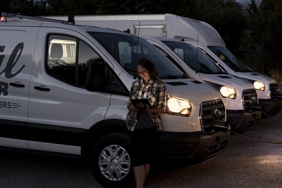 Woman leans against an 2023 Ford E-Transit™ van with a tablet in her hand