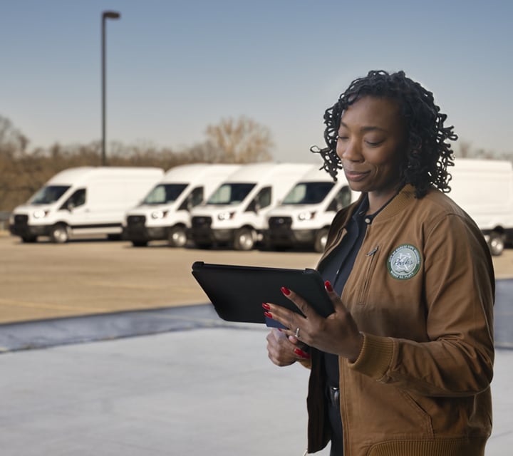 Woman standing with a clipboard with a fleet of 2023 Ford E-Transit™ vehicles in the background