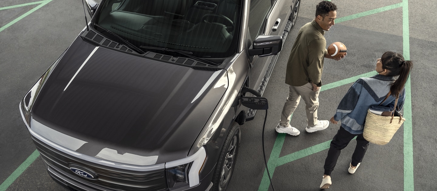 A man and woman walk away from an F-150® Lightning® parked in a public charging space