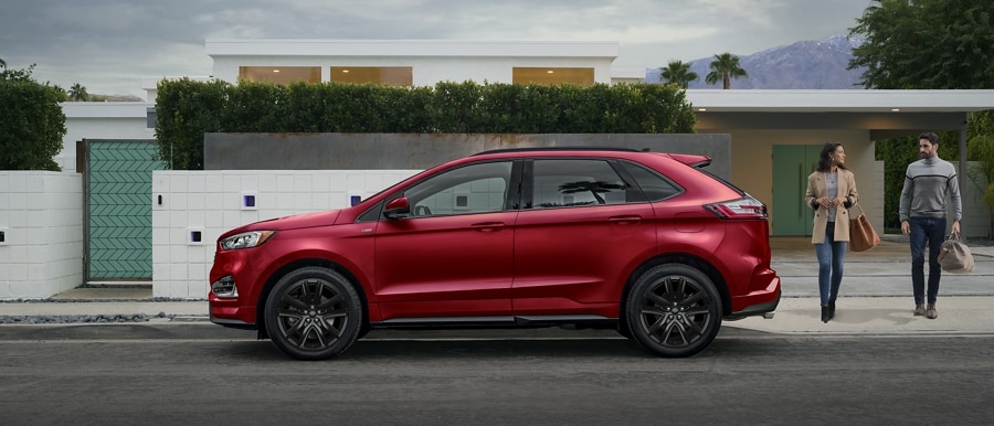 2023 Ford Edge® ST-Line model in Rapid Red parked in front of a modern home with a man and woman approaching