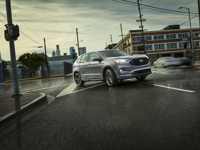 A 2023 Ford Edge® ST SUV in Iconic Silver being driven on a wet city road