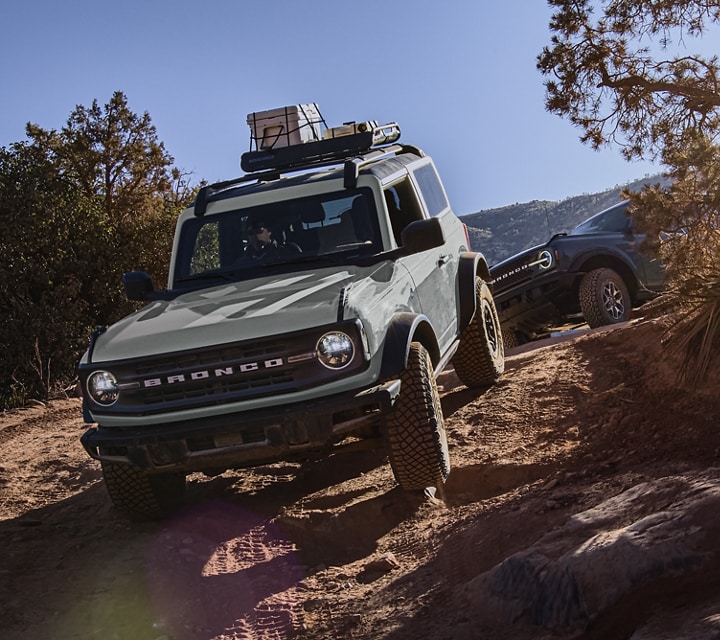 Four-door 2023 Ford Bronco® Everglades™ model driving down a rocky mountain