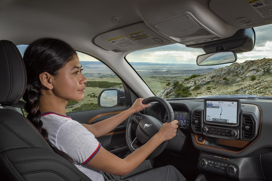 Woman sitting in a Ford 2024 Ford Bronco® Sport with hands on the steering wheel looking at a map on the interior screen