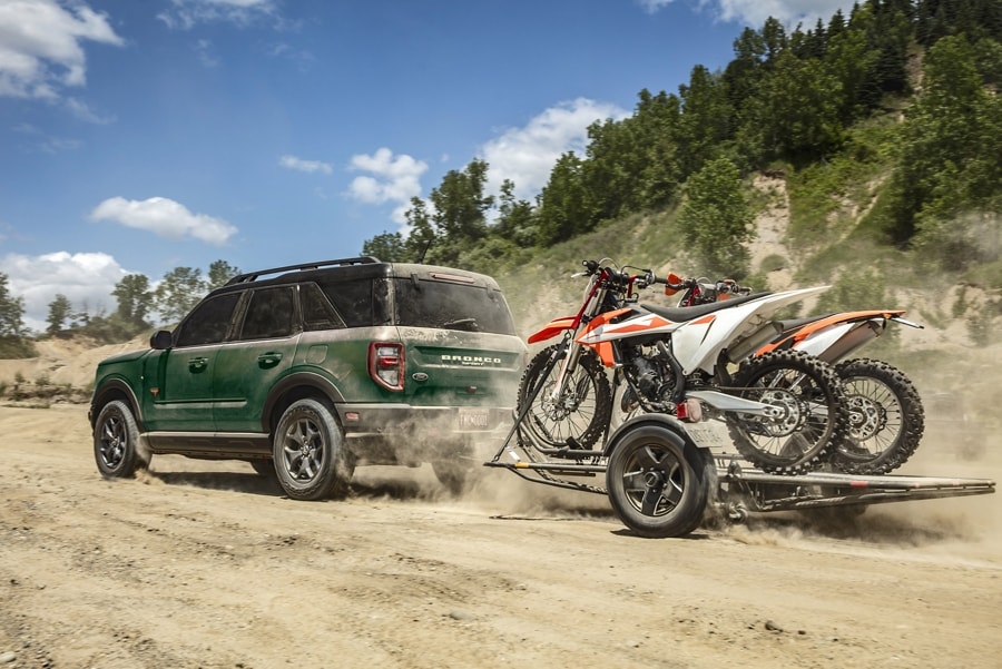 A 2024 Ford Bronco® Sport being driven, pulling a trailer with motorcycles on the back