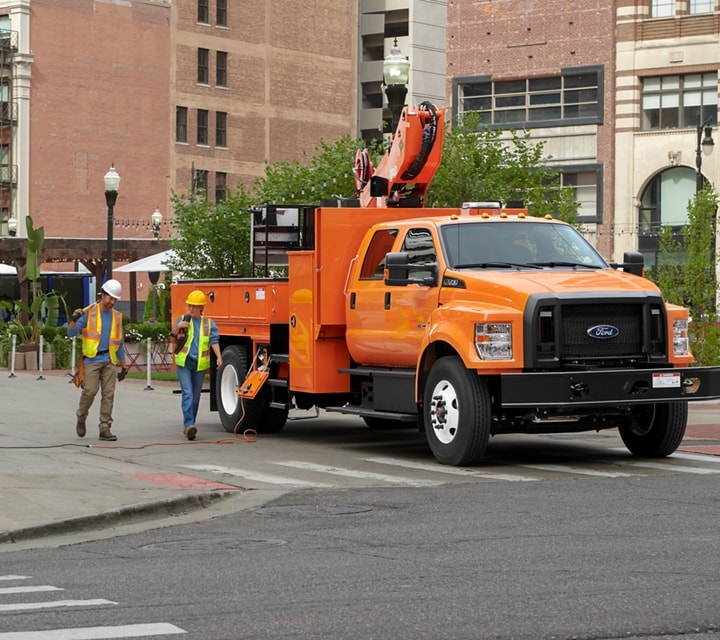 Workers walking near 2024 Ford F-750 Crew Cab in Tangier Orange with aerial lift upfit