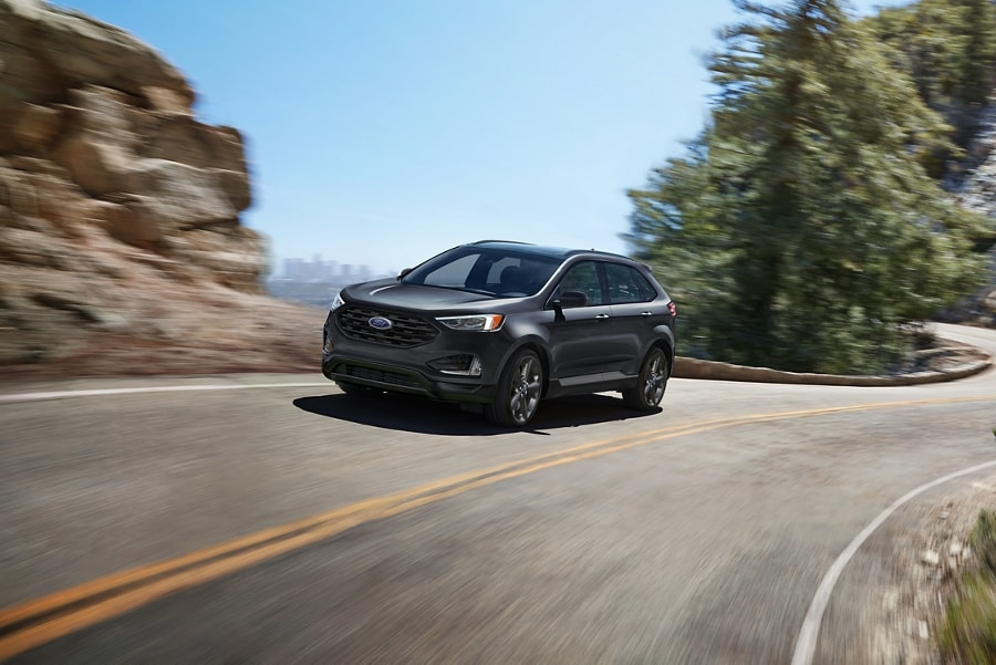 2023 Ford Edge® SEL in Carbonized Gray being driven on a curvy road with city in background