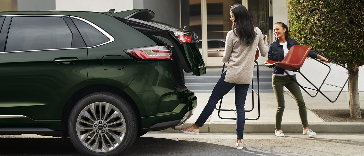 Two women holding chairs stand behind a 2023 Ford Edge as one operates the hands-free liftgate