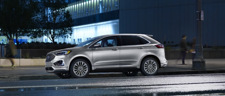 2023 Ford Edge® Titanium SUV in Iconic Silver being driven on a city street at night
