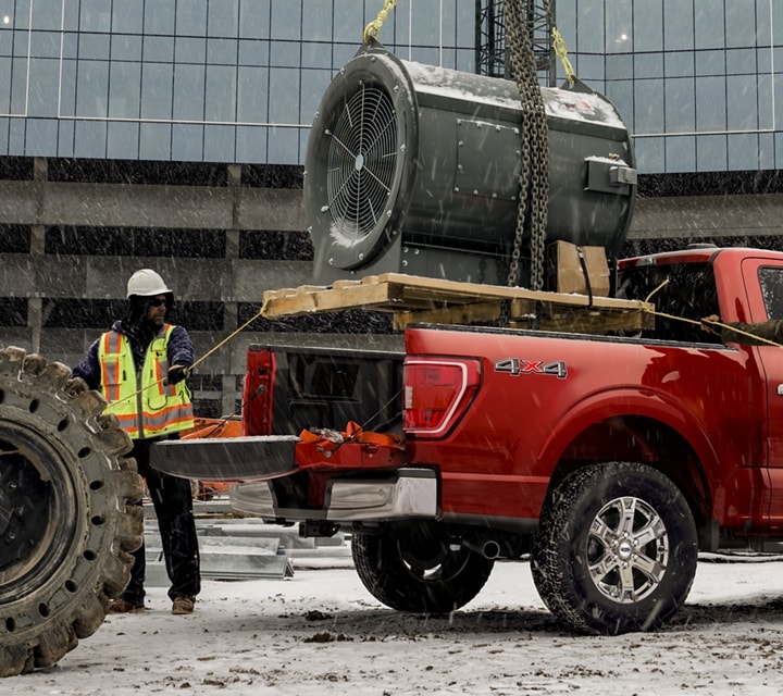 Two men help guide a turbine engine into the bed of a 2023 Ford F-150® pickup