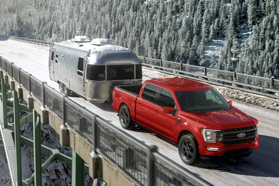 2023 Ford F-150® pickup pulling a camper trailer over a mountain bridge