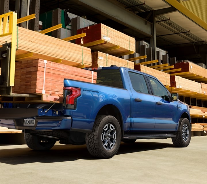 A blue 2023 Ford F-150® Lightning® parked on a worksite. The bed is loaded with two by fours and other lumber