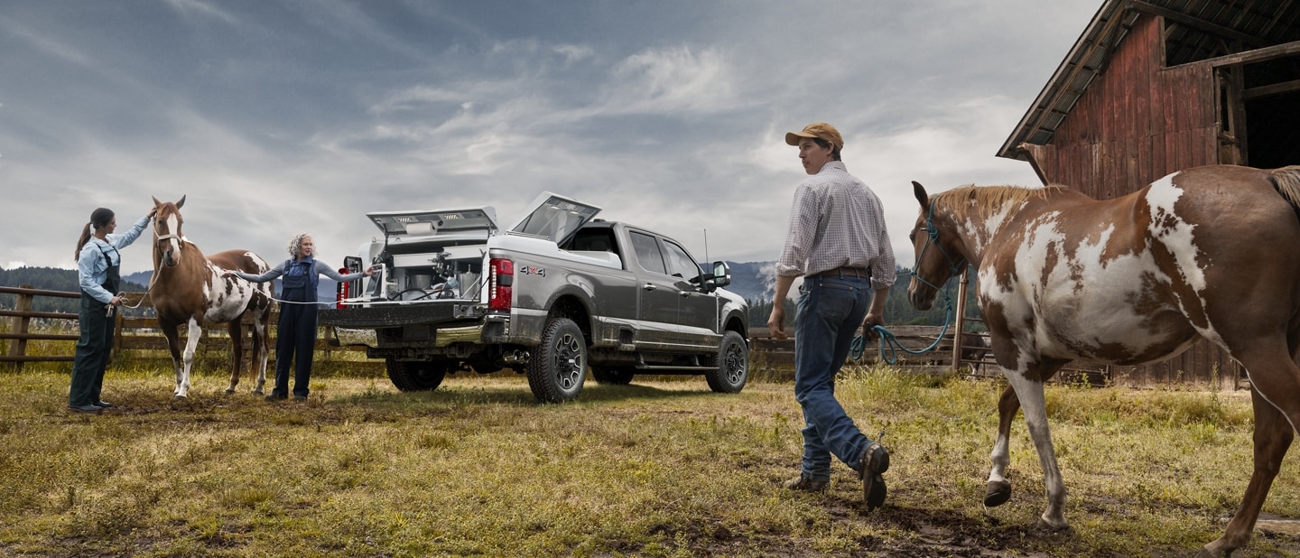 Man walking with a horse toward two women standing at the rear of a 2023 Ford Super Duty® F-250® Platinum pickup