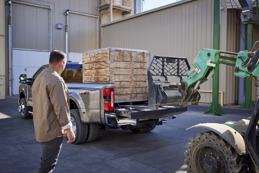 Man watching a hi-low load a crate into the bed of a 2023 Ford Super Duty® pickup