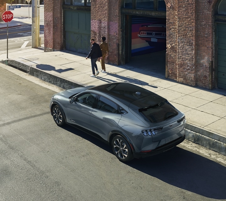 Woman walking with man who looks back at a 2023 Ford Mustang Mach-E® SUV parked on a city street