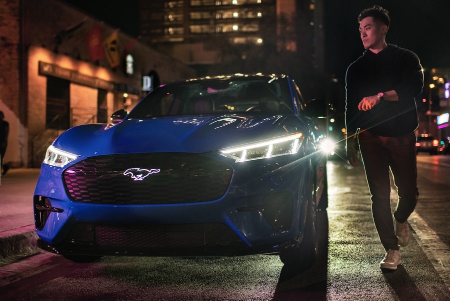 Man walking up to a 2023 Ford Mustang Mach-E® SUV with illuminated Pony graphic and headlights at night