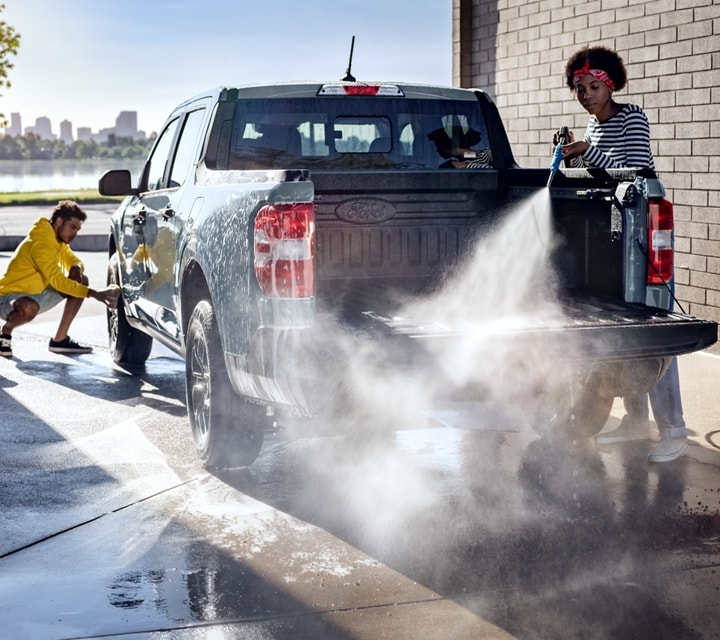 A 2024 Ford Maverick® truck in Azure Gray Metallic is being sprayed with water by two people at an outdoor carwash