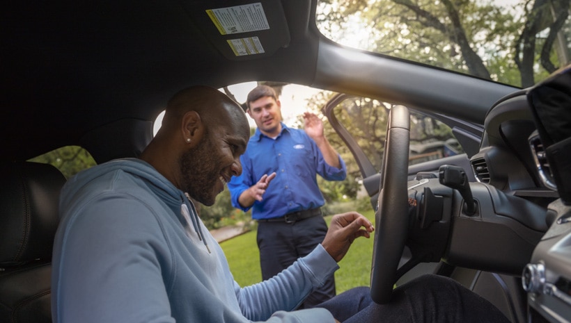 A man sitting in a vehicle is talking to a service technician