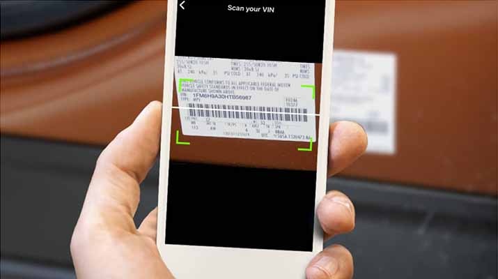 A hand holding a smartphone scanning the barcode for a Vehicle Identification Number.
