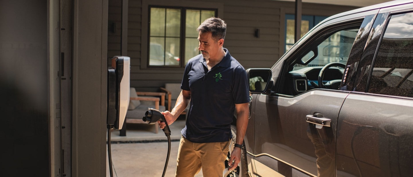 A man using a Ford Charge Station Pro to plug in a 2023 Ford F-150® Lightning®