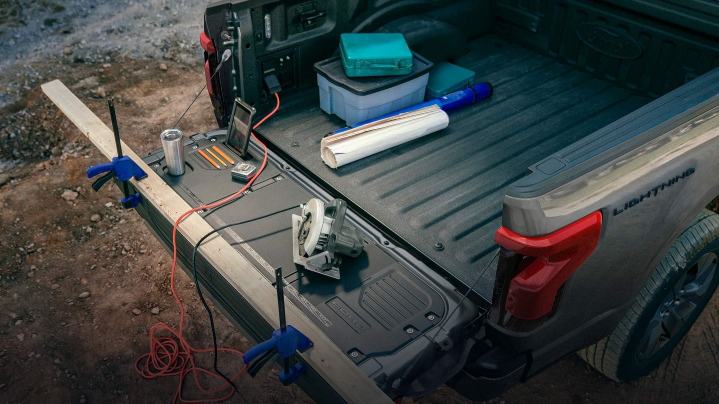 The bed of a 2023 Ford F-150® Lightning®. Its tailgate is open with construction tools positioned around the mobile work surface