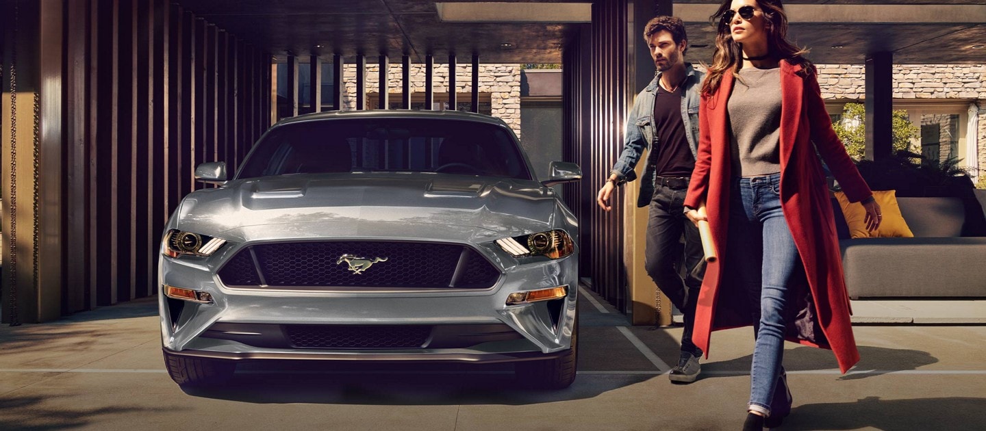 2023 Ford Mustang® coupe in Carbonized Gray Metallic parked in a carport with two people walking away