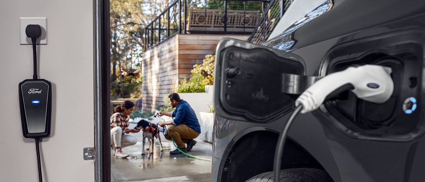 A 2022 Ford F-150® LightningTM being charged inside a garage next to two people washing a dog