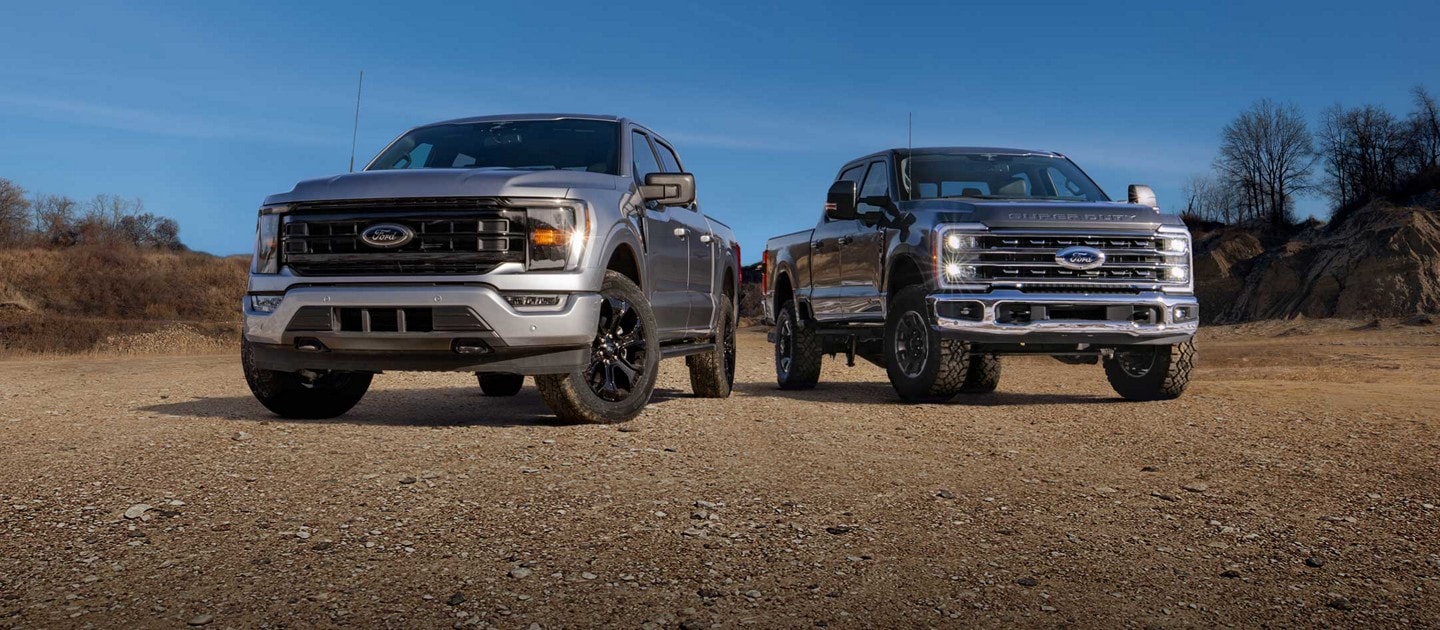 Two silver 2023 Ford pickup trucks parked on an unpaved road