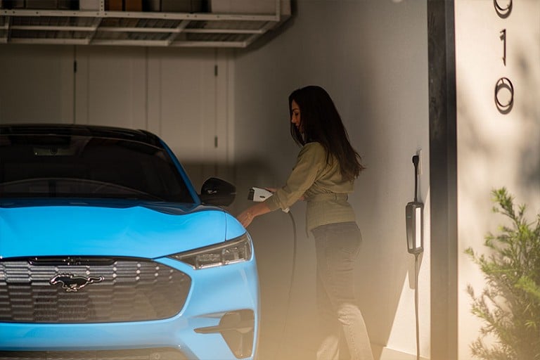 Woman in a garage holding a Ford Mobile Charger beside a 2023 Ford Mustang Mach-E® SUV
