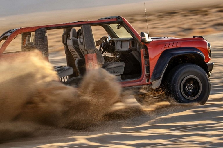 A 2023 Ford Bronco® Raptor® in Code Orange with doors removed being driven through sand dunes