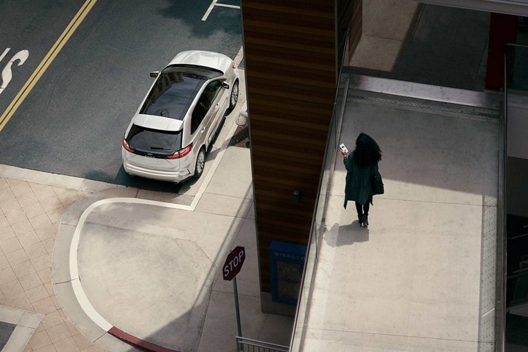 Woman holds a smartphone on a walkway overlooking her 2023 Ford Edge® parked on the street below