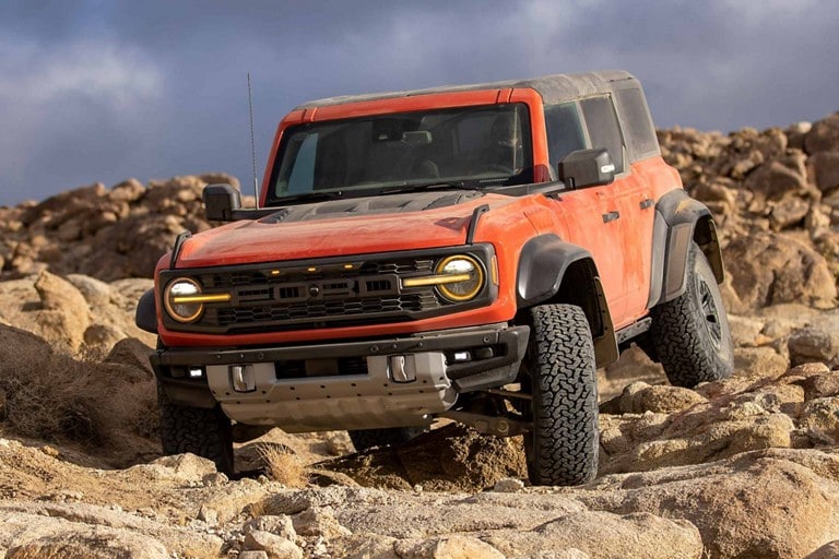 Four-door 2023 Ford Bronco® Raptor® in Hot Pepper Red (extra cost paint) being driven over rocks