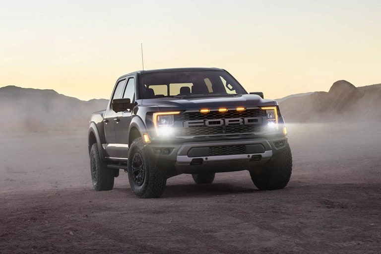 A 2022 Ford F-150® Raptor® being driven at dusk with headlights on