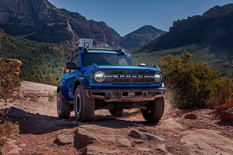 A two-door 2023 Ford Bronco® Black Diamond® in Velocity Blue being driven on a trail
