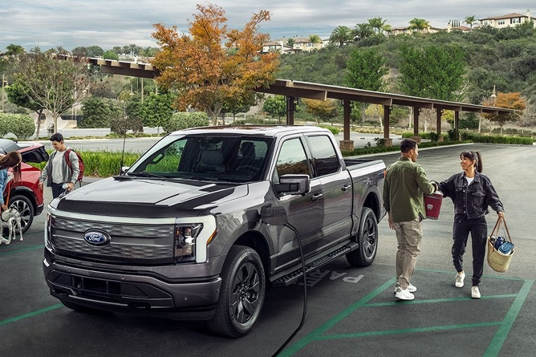 A 2022 Ford Mustang Mach-E® and a Ford F-150® LightningTM are being charged at a charging station with people