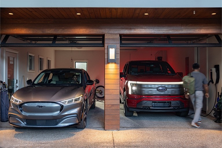 A 2023 Ford Mustang® Mach-E® leaves a home garage while a 2023 Ford F-150® Lightning® charges
