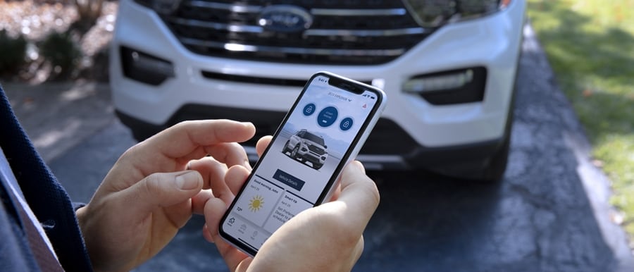 A man stands in front of a white Ford Explorer holding a smartphone displaying the FordPass™